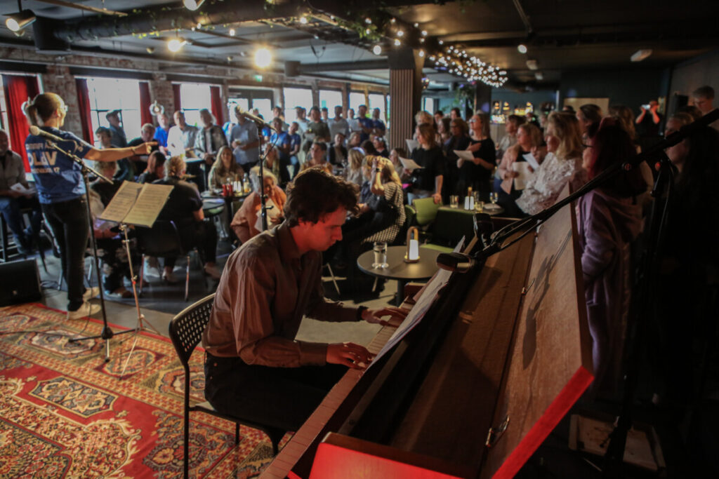 Bilde av et lokale med folk som synger og noen som spiller piano